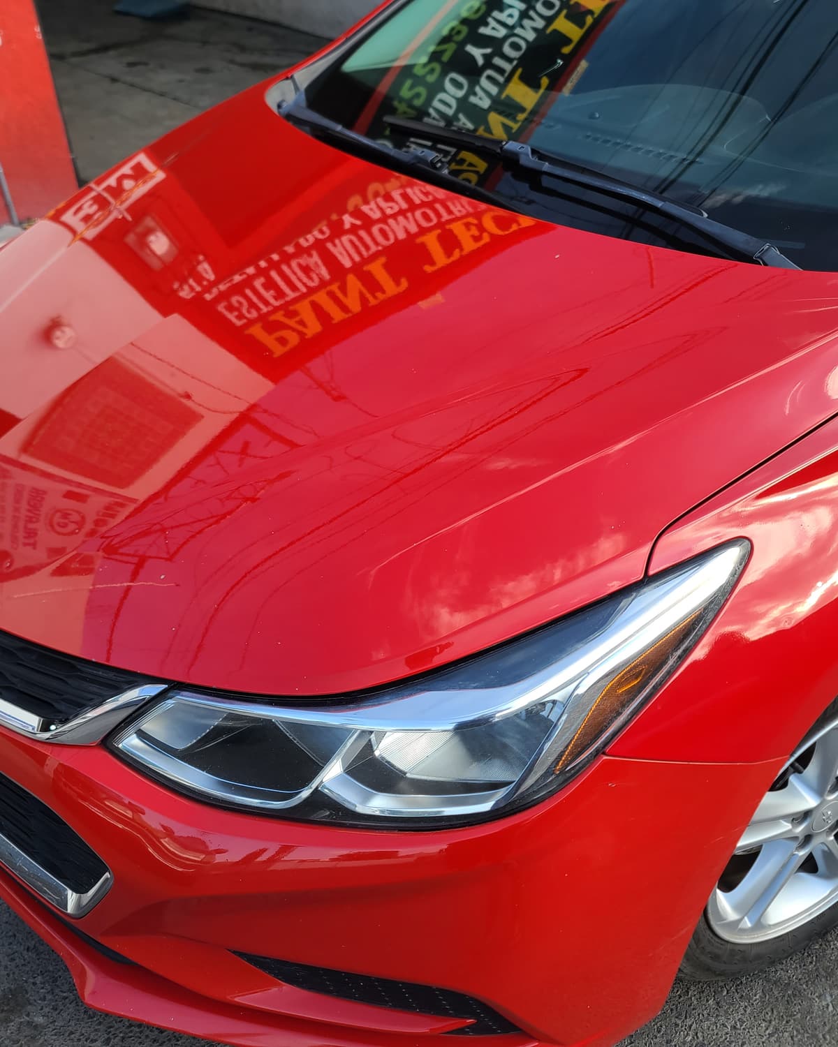 Auto rojo recién pulido frente al taller; el cofre refleja el letrero de Paint Tech Inc