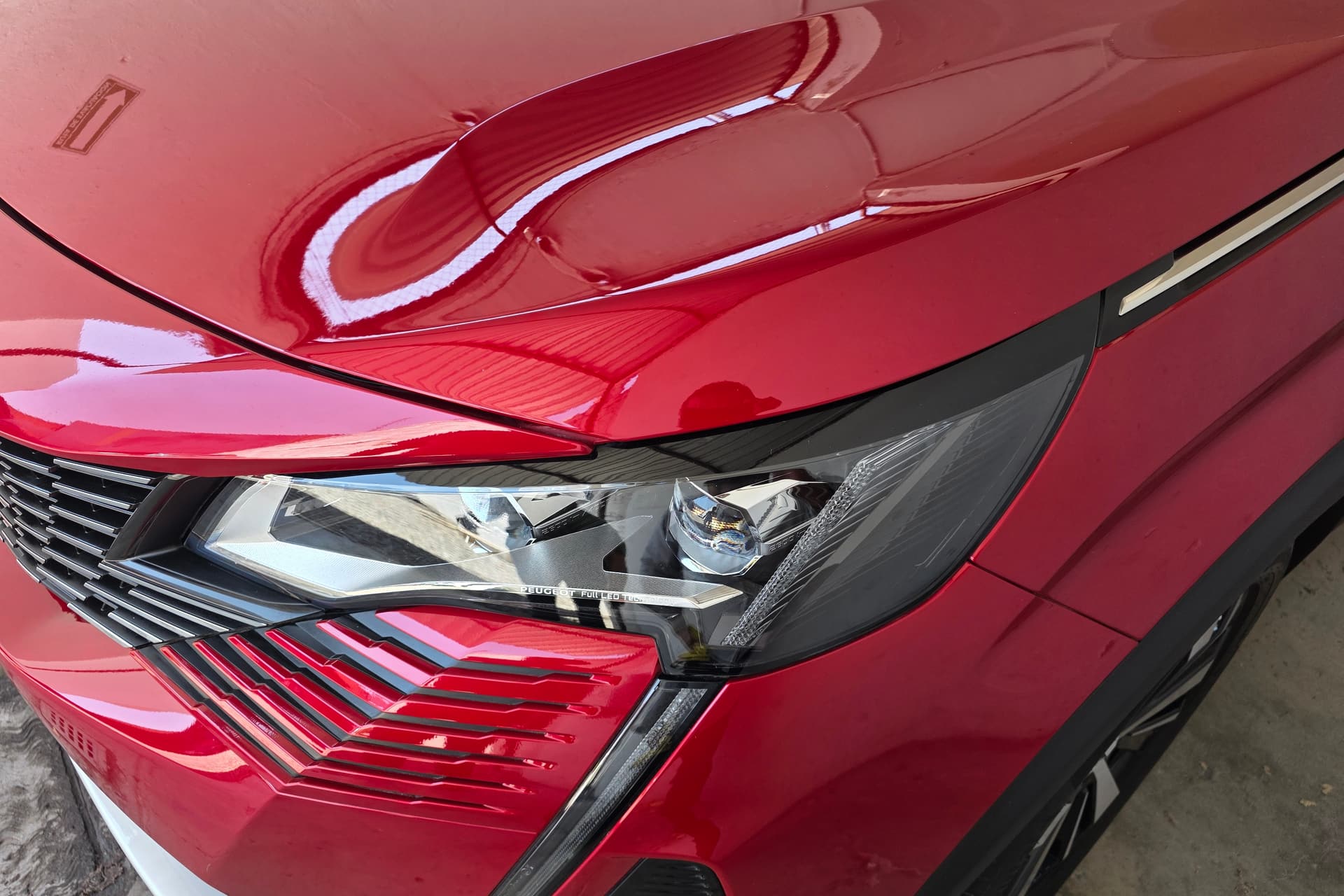 Cofre y faro de un auto rojo con la pintura recién pulida, reflejando el techo del taller